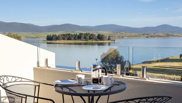 Eine Terrasse mit Tisch für zwei Personen, Blick auf einen See mit Bergen im Hintergrund.