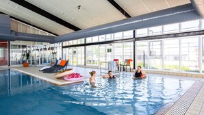 Ein Innenpool mit klaren Glaswänden, Liegestühlen und Blick ins Freie.