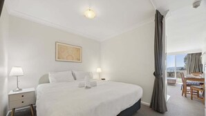 Une chambre d’hôtel avec un grand lit, des tables de chevet, un tableau au mur et un balcon avec une table et des chaises.