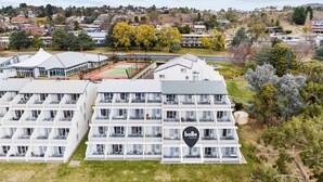 Un hôtel à plusieurs étages au design moderne, doté de balcons à chaque niveau, d’un court de tennis et offrant une vue sur le quartier environnant.