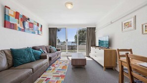 Un salon moderne avec un canapé, une table basse, un téléviseur et une vue à travers la porte vitrée.