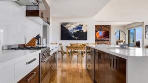 A modern kitchen with a central island, wooden chairs, a large painting, and a stone wall backsplash.
