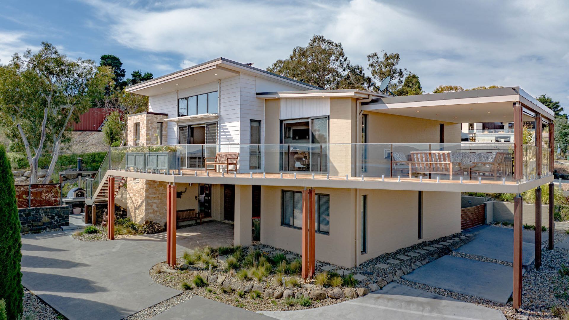 Une maison moderne à deux étages, dotée d’un balcon, de fondations en pierre et d’un espace patio.
