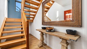 A wooden staircase with a mirror above it, a wooden console table with bowls, and a red door in the reflection.