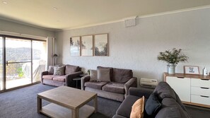 Un salon spacieux avec une grande fenêtre, un ensemble de canapés, une table basse et un meuble blanc.