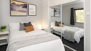 A modern bedroom with a large bed, a smaller bed, a mirror, and artwork on the walls.