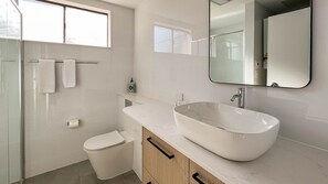 Een moderne badkamer met een groot wit wastafelmeubel, een douchecabine van glas en een toilet.