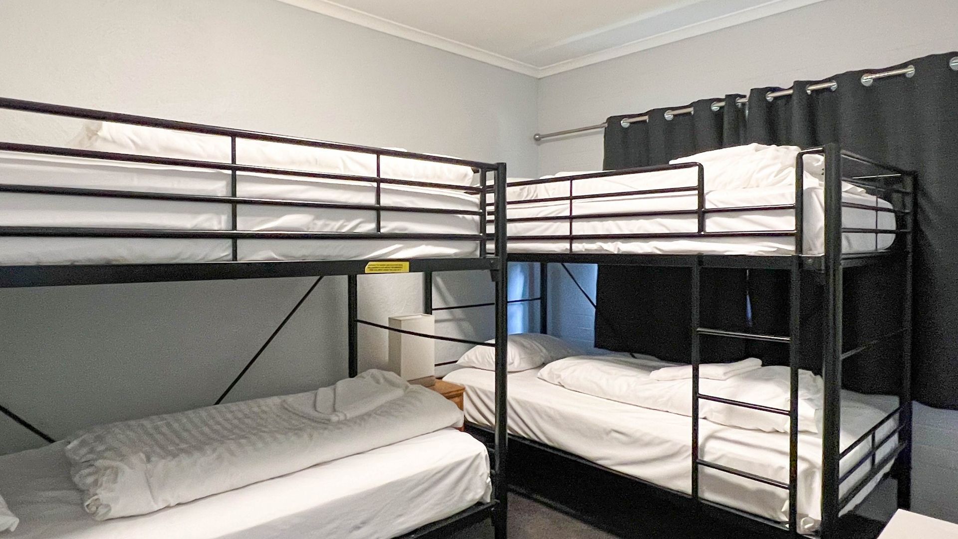 A bunk room with three bunk beds, a small table, and a window with curtains.