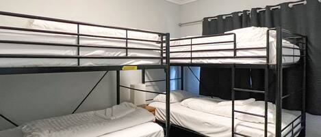 A bunk room with three bunk beds, a small table, and a window with curtains.
