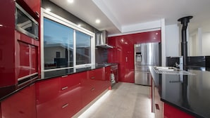 A modern kitchen with red cabinetry, stainless steel appliances, and a black countertop.