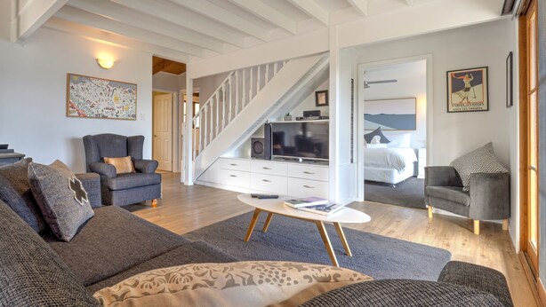 A spacious living room with a staircase, a sofa set, a coffee table, and a bedroom visible through an open door.