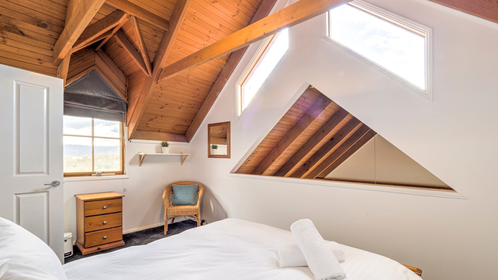 Een slaapkamer met een schuine kap, een bed, een dressoir, een stoel en een raam.