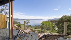 A wooden deck with two striped lounge chairs, a view of a lake, and distant mountains.