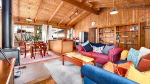 Una sala de estar acogedora con techo de madera, un sofá rojo, un sofá azul y un comedor con mesa y sillas.