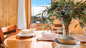 Una mesa de madera con vistas al exterior, un florero con follaje y un cuenco sobre la mesa.