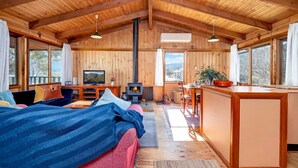 Un interior de cabaña acogedor, con paredes de madera, una chimenea, un comedor y ventanas amplias.