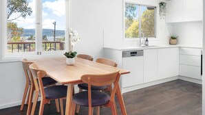 Une cuisine moderne avec une table et des chaises en bois, des meubles blancs et une vue sur l’extérieur.