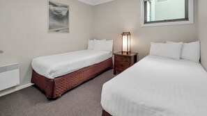 A hotel room with two beds, a bedside table with a lamp, a radiator, and a framed picture on the wall. - Jasper 1 is spacious and modern apartment located conveniently in the middle of the Jindabyne. (Jindabyne)