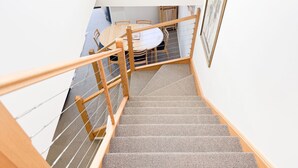 A wooden staircase with a textured carpet, leading to a dining area with a round table and chairs. - Angala 2 located across from Friday Flat (Thredbo)