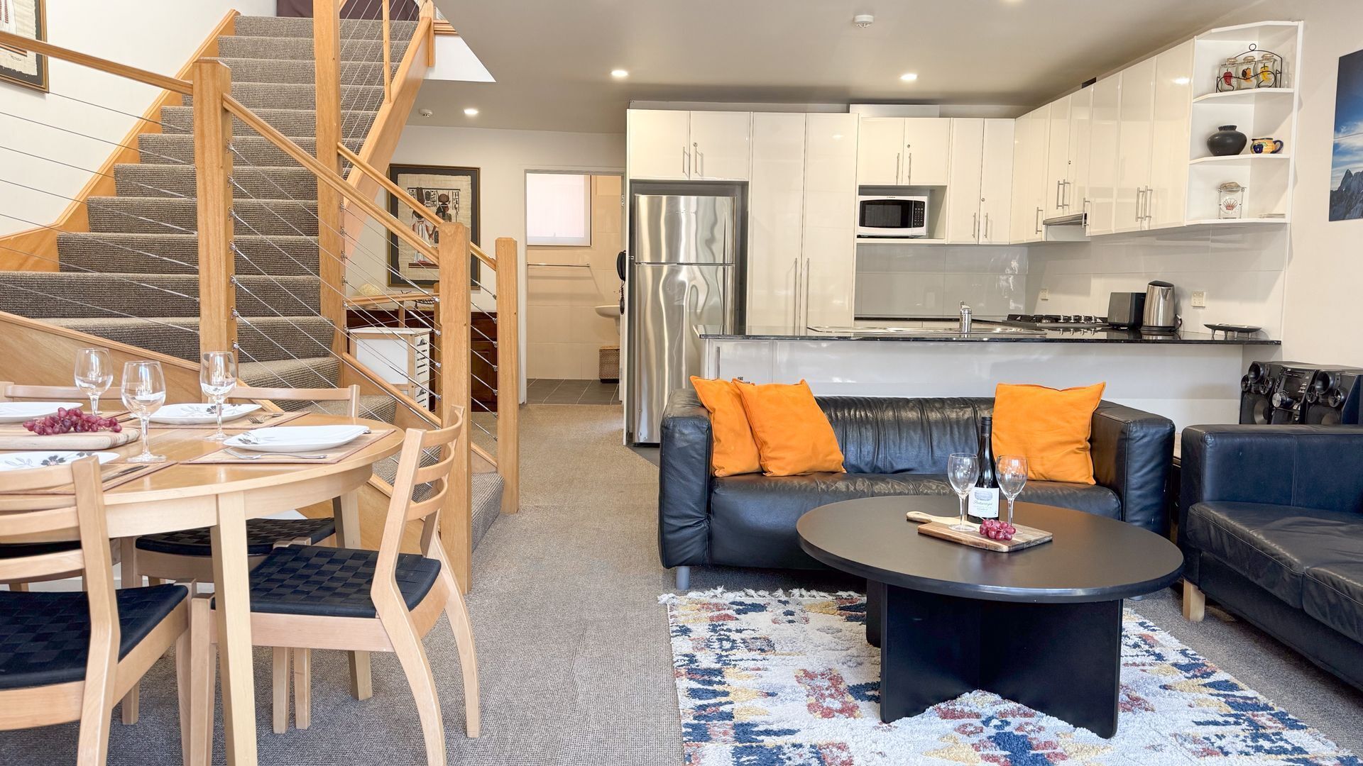 A modern living space with a staircase, a dining area, a sofa set, and a kitchen.