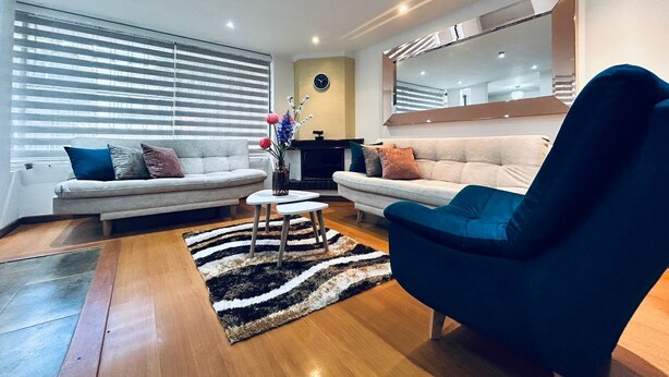 A modern living room with two sofas, a coffee table, and a blue armchair. - Spacios Grand Park 93 (Bogotá)