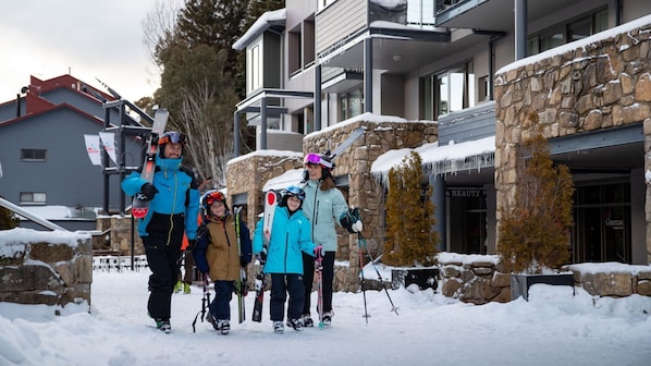 A family with skis and snowboards walking towards a building with stone walls and a sign reading "BEAUTY".