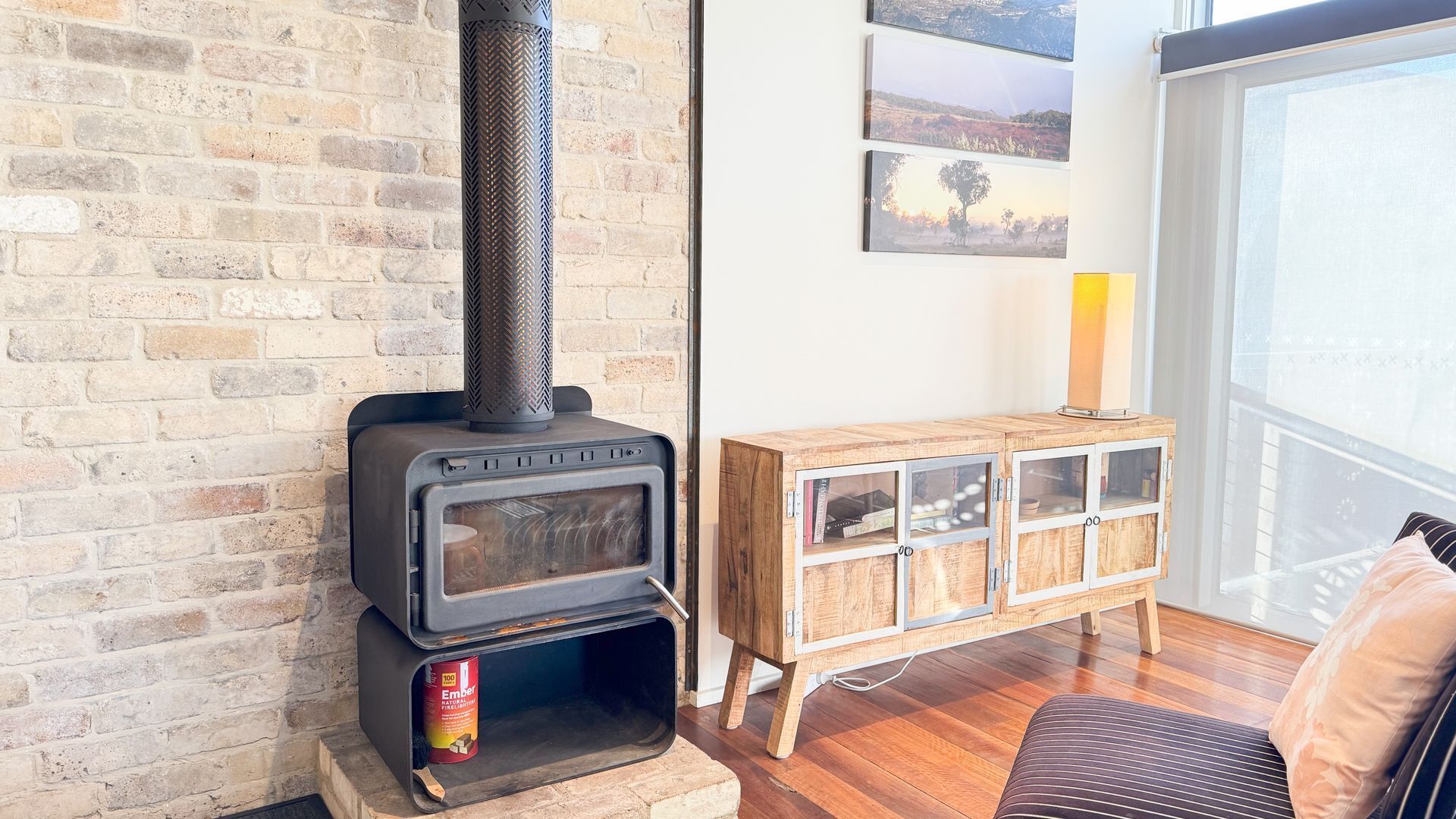 A wood-burning stove with a chimney, a wooden cabinet with glass doors, and a view of the outdoors through a large window.