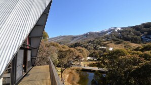 A building with a corrugated metal roof overlooking a valley with a river and snow-capped hills.