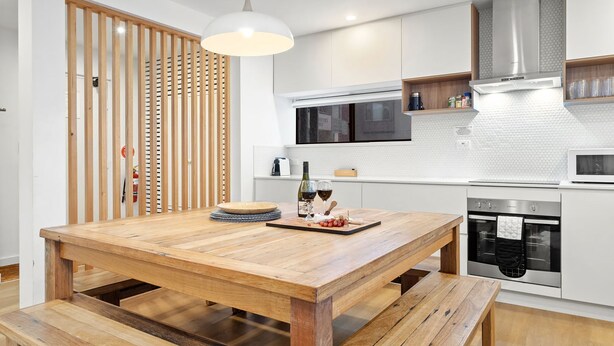A modern kitchen with a wooden dining table, a built-in oven, and a microwave.