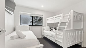 A bedroom with two bunk beds, a window with a view of trees, and a bedside table with a lamp.