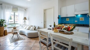 Una cocina moderna con azulejos azules, un comedor con mesa y sillas blancas, y una sala de estar acogedora con sofá y cortinas.