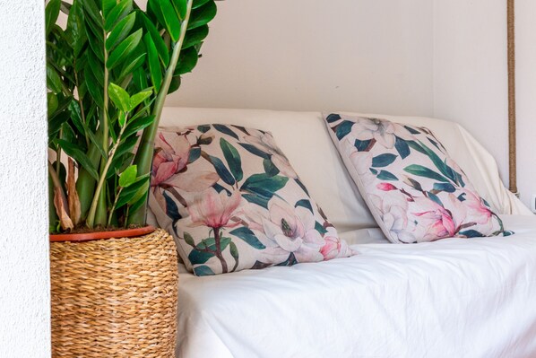 A wicker basket with a plant, two pillows with a floral pattern, and a white sofa. - Independent flat Via del Mare 34 centre Villasimius (Villasimius)