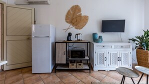 Una cocina compacta con refrigerador, microondas y cafetera sobre una mesita. Un televisor de pantalla plana está montado en la pared, encima de un mueble.