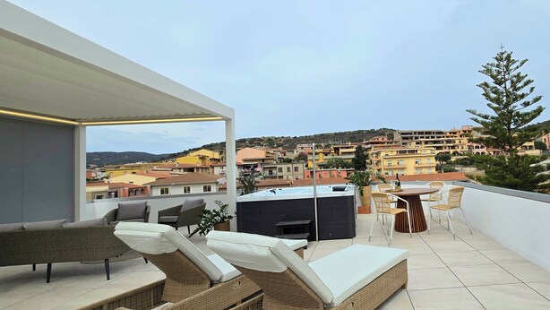 Terraza en la azotea con mobiliario de mimbre, una parrilla y vistas a un pueblo en la colina.