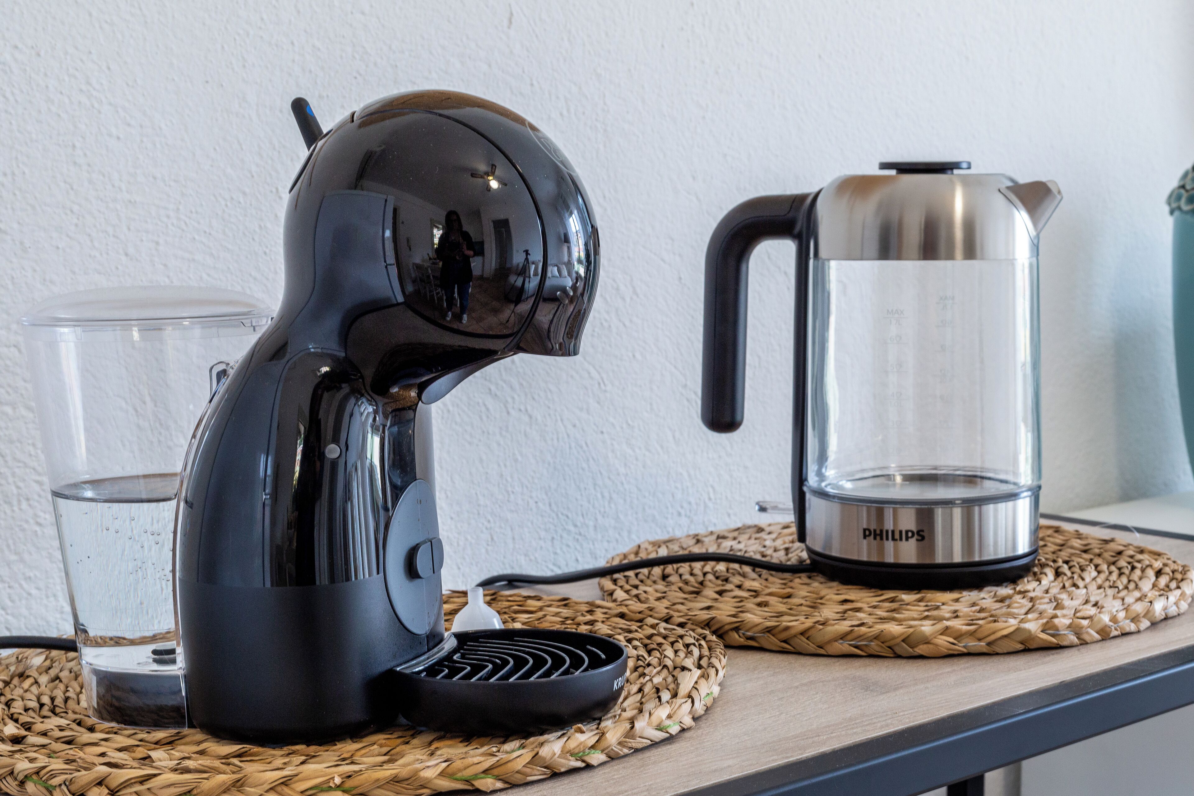 A coffee maker and a water kettle on a woven placemat.