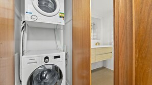 Un lavadero pequeño y funcional con lavadora y secadora de carga frontal, una puerta de madera y una pequeña encimera con artículos de aseo.