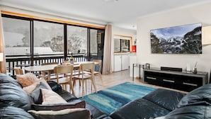 Una sala de estar moderna con un televisor grande, un comedor y una cocina al fondo.