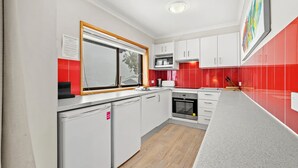 Una cocina moderna con armarios blancos, un salpicadero rojo y una ventana con persianas.