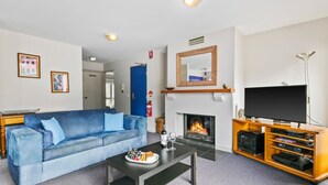 Un salon avec un canapé bleu, une table basse sur laquelle sont posés des en-cas, une cheminée, un téléviseur et une bibliothèque.