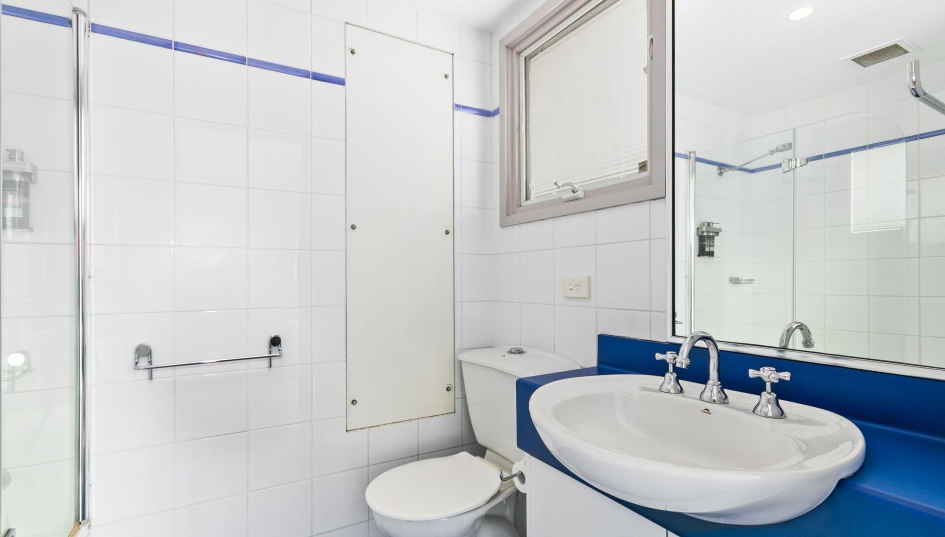 A bathroom with a white toilet, a sink with a blue countertop, and a shower area.