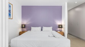 A bedroom with a large bed, two bedside tables with lamps, a wardrobe, and a framed picture on the wall.