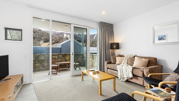 A modern living room with a sofa, coffee table, and a view of a mountainous landscape through a sliding glass door.