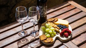 A wooden table with a cheese board, grapes, strawberries, and crackers. Two wine glasses and a bottle of wine are also visible.
