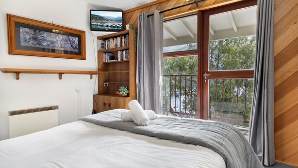 Ein Schlafzimmer mit einem Bett, einem Bücherregal, einem Fernseher und einem großen Fenster mit Vorhängen.