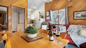 Ein gemütliches Wohnzimmer mit einem Holzesstisch, einem roten Sofa und einem großen Fenster mit Blick auf Bäume.