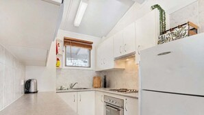Eine moderne Küche mit weißen Schränken, einem Edelstahl-Kühlschrank, einem Backofen und einem Fenster mit Jalousien.