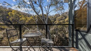 Un balcón con una mesa y dos sillas, con vista a un paisaje natural de árboles y colinas.