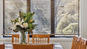 Un comedor con una mesa y sillas, un jarrón con flores y una ventana con persianas.