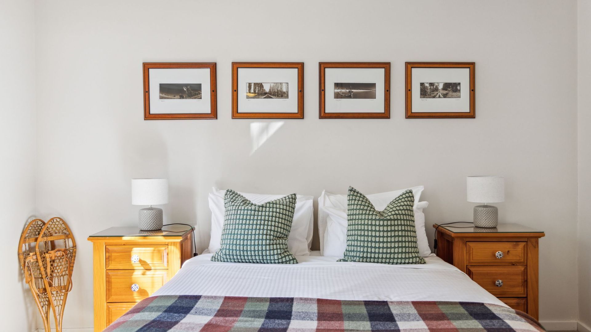 Une chambre à coucher bien rangée, avec un lit, deux tables de chevet dotées de lampes, une petite table en bois et un mur orné de quatre tableaux encadrés.