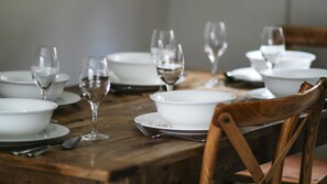 A wooden dining table with white plates, bowls, and wine glasses.